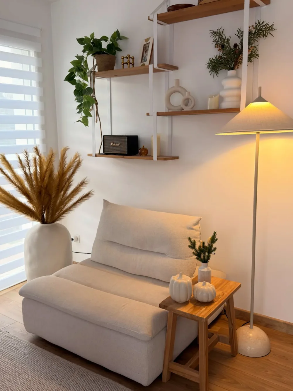 Small living room with a cream sofa, wood side table, open shelving, and neutral decor