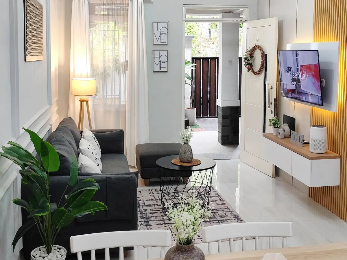 Small living room with a compact gray sofa, round coffee table, wall-mounted TV, white furniture, and natural wood accents.