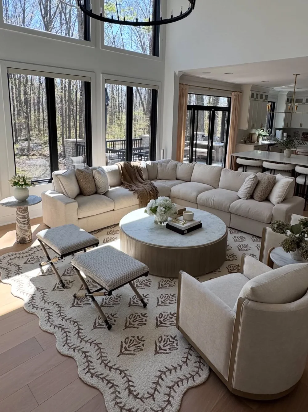 Open-concept living room with a cream sectional, round coffee table, and tall windows overlooking trees