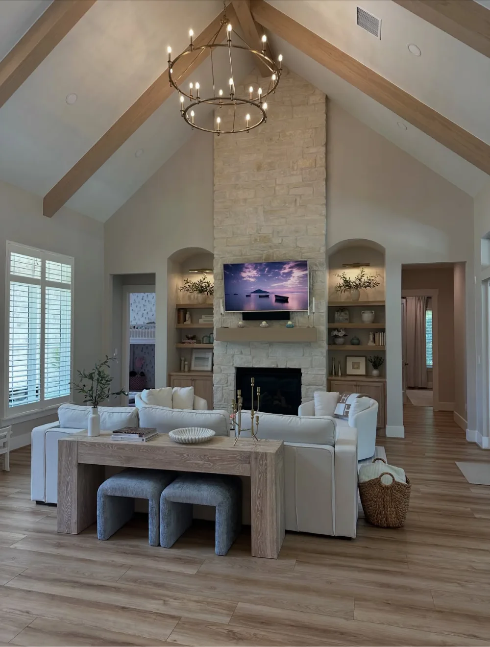 Open living room with white sofas, stone fireplace, built-in shelves, and vaulted ceiling