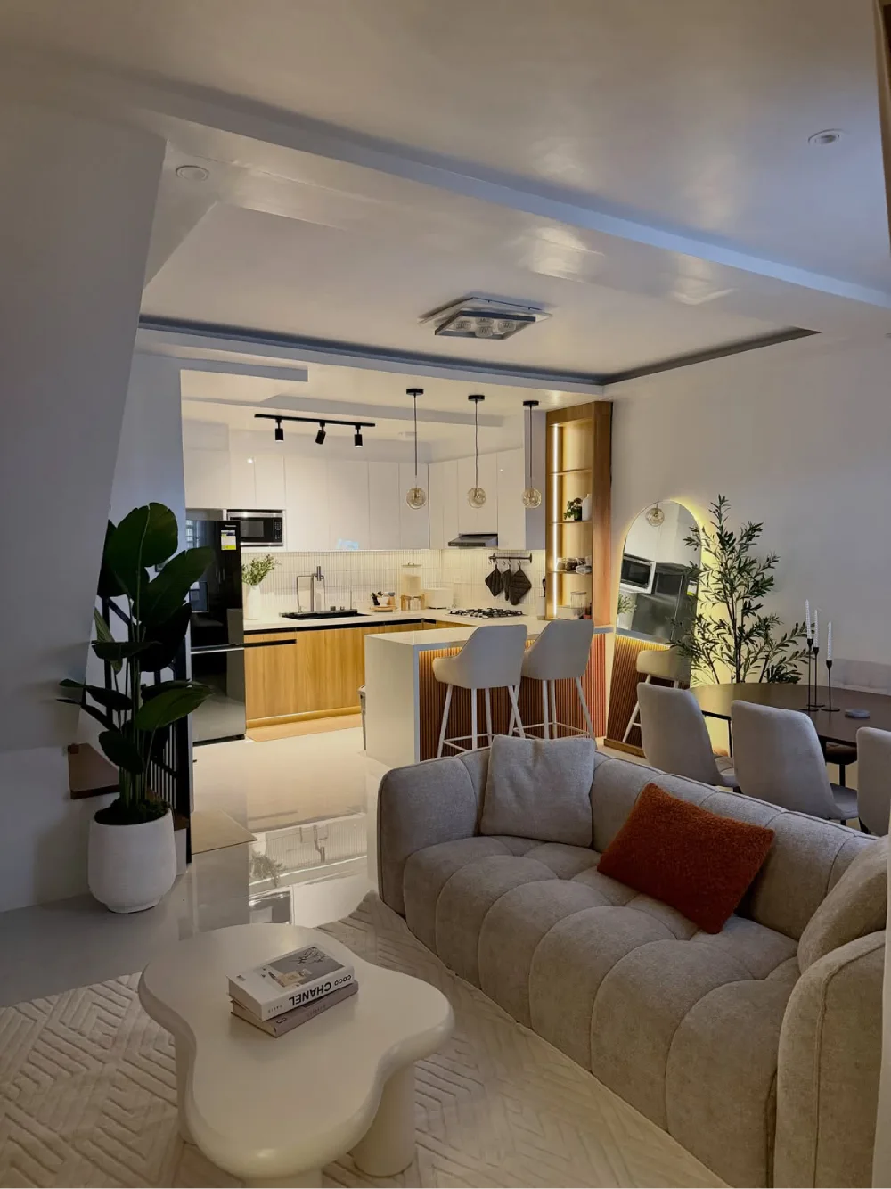 Open-concept living room with cream sofa, kitchen island, dining area, and warm wood accents