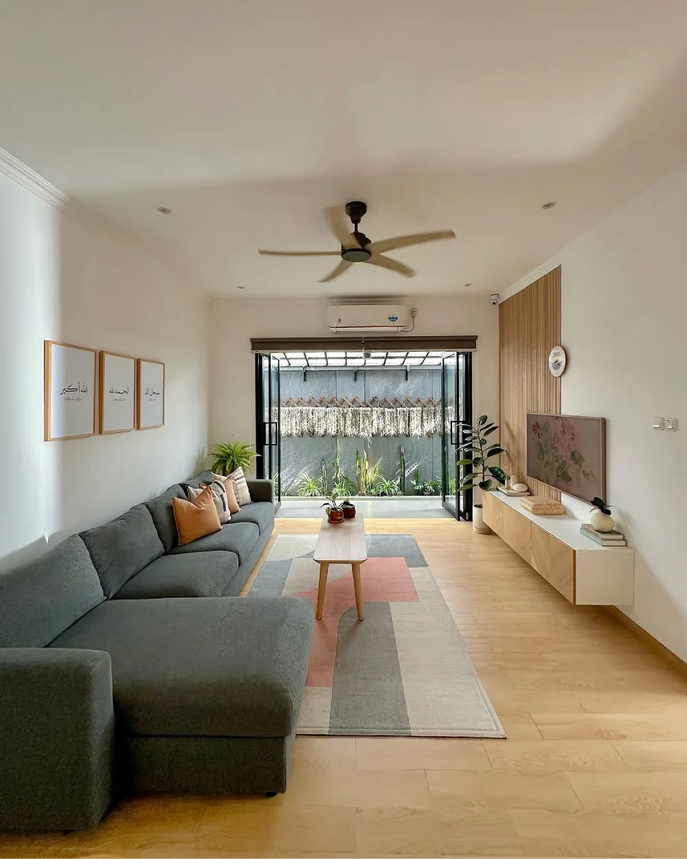 Open living room with gray sectional, geometric rug, wood TV console, and garden view
