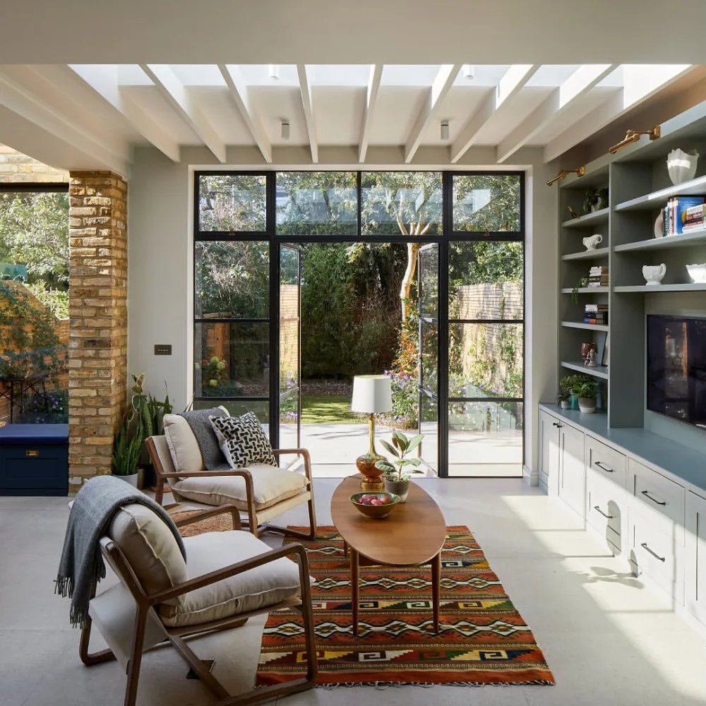 Living room seating with colorful patterned rug, wood chairs, and garden view