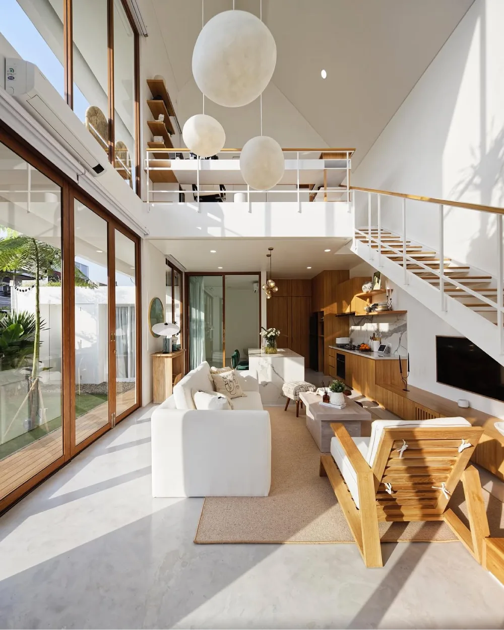 Double-height open-concept living room with white furniture, wood kitchen cabinetry, and staircase
