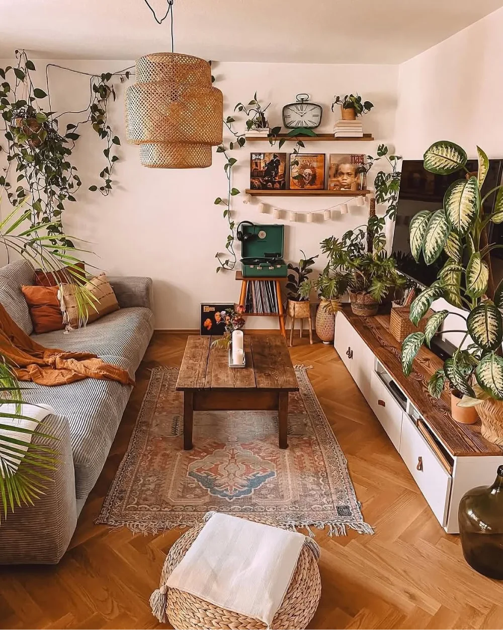Plant-filled earthy living room with rattan pendant, vintage rug, wooden coffee table, and greenery