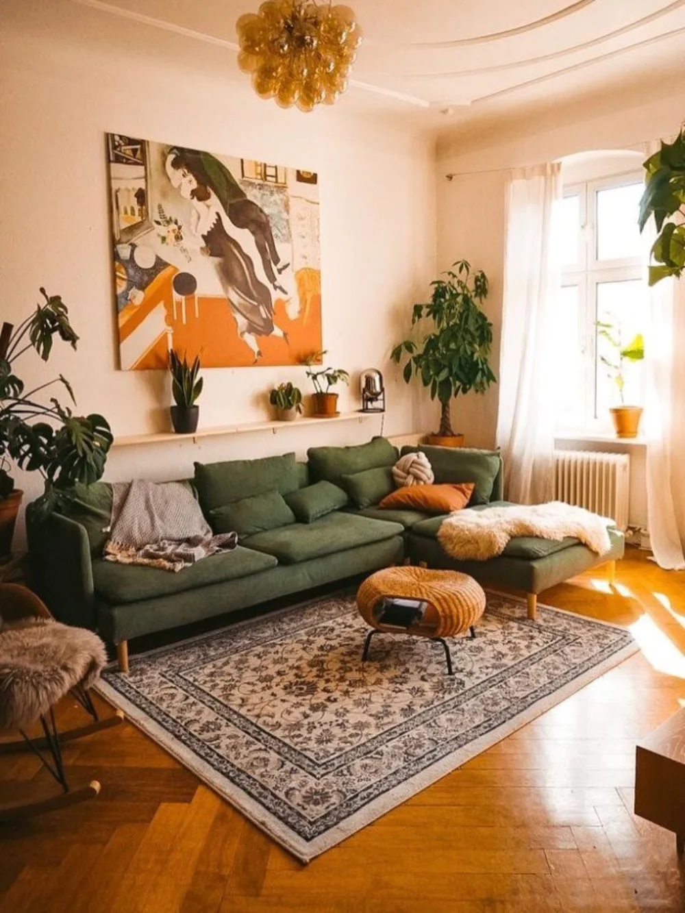 Earthy living room with a deep green sectional sofa, patterned rug, plants, and warm wood floors