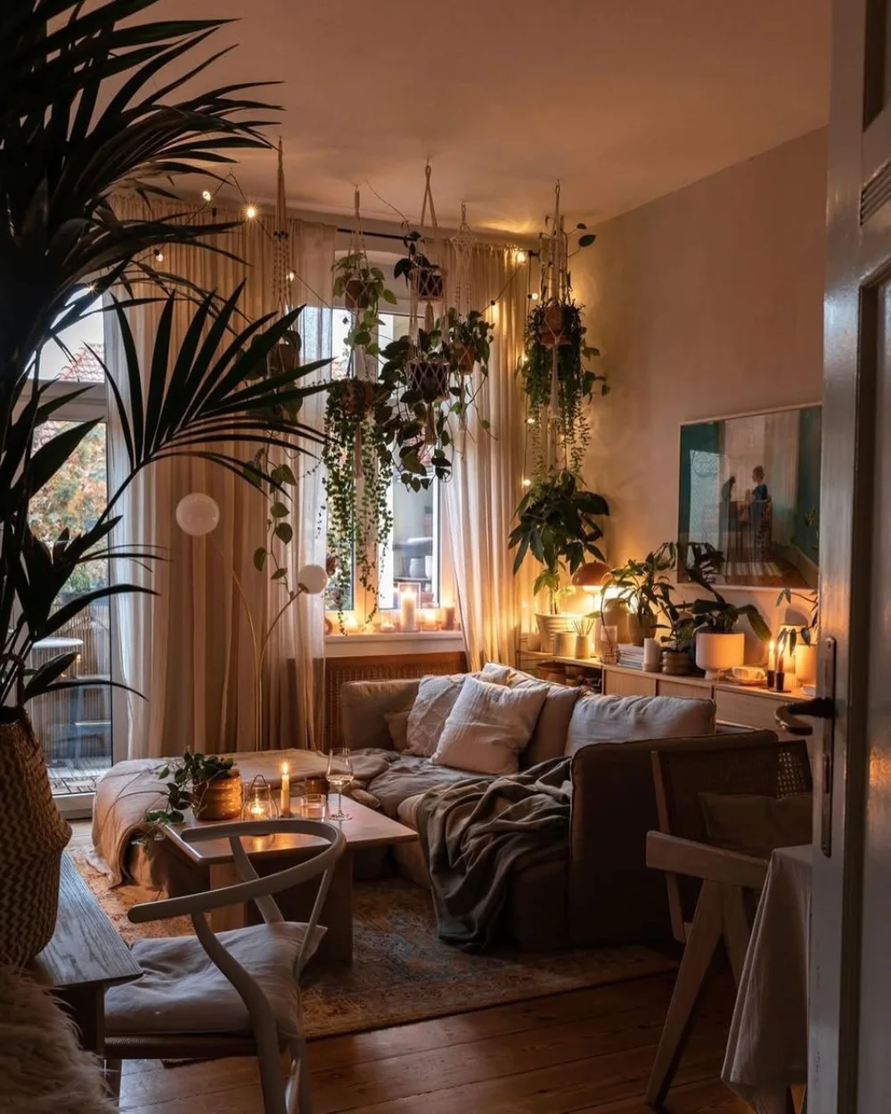 Moody earthy living room filled with hanging plants, candles, warm lighting, and natural wood furniture