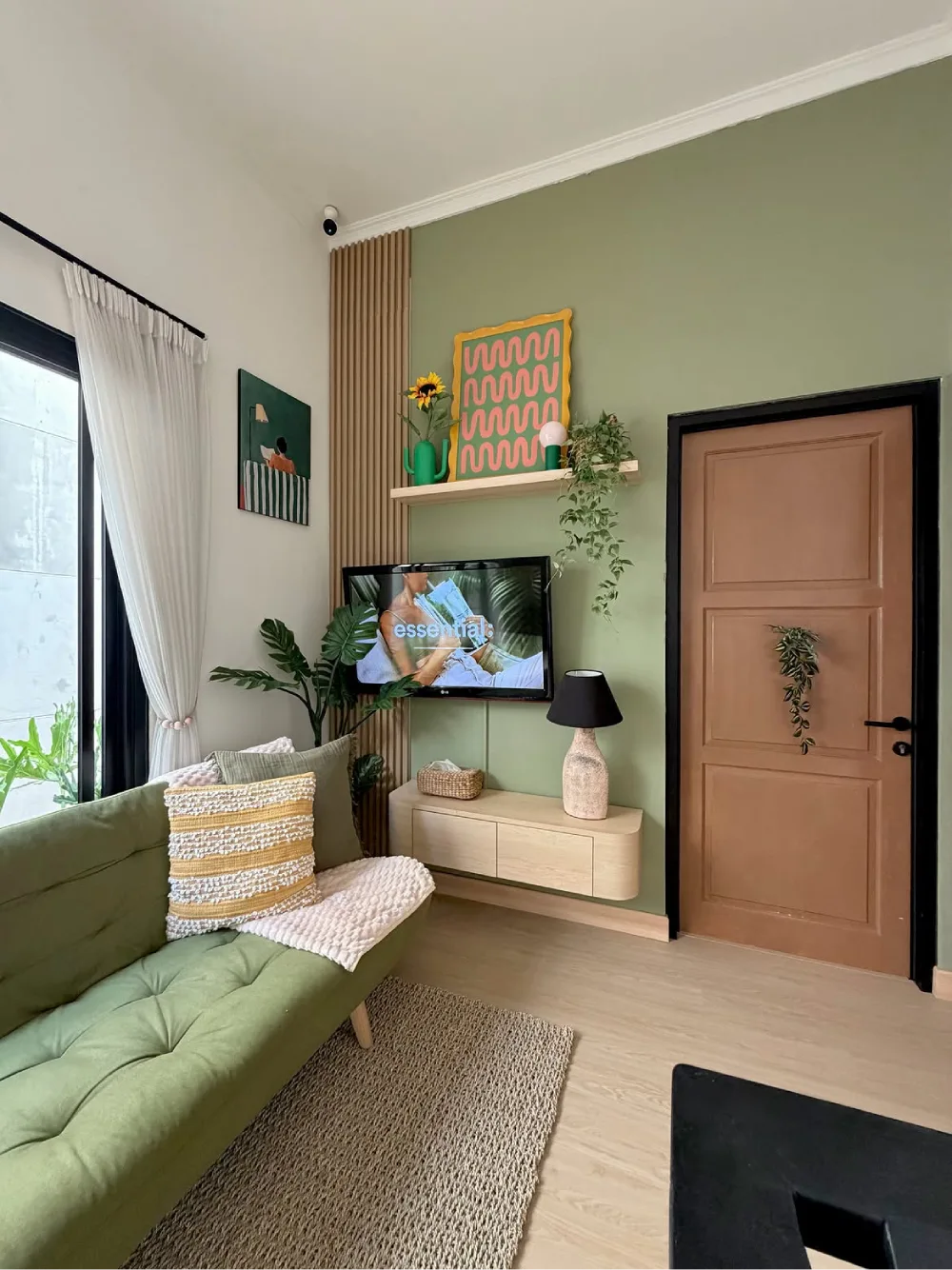 Sage green living room with a green sofa, natural wood accents, plants, and colorful wall art