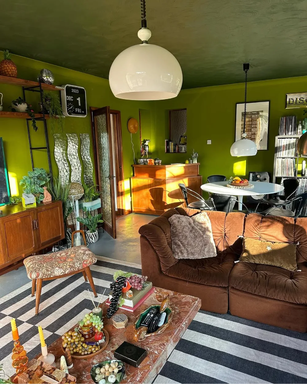 Lime green living room with brown velvet sofa, wooden furniture, indoor plants, and striped rug