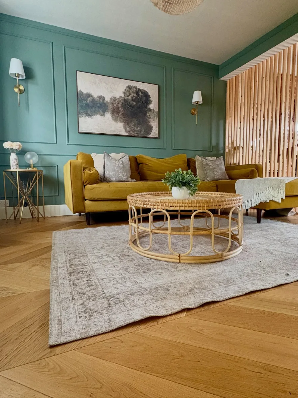 Teal green living room with mustard sofa, rattan coffee table, wood paneling, and botanical artwork