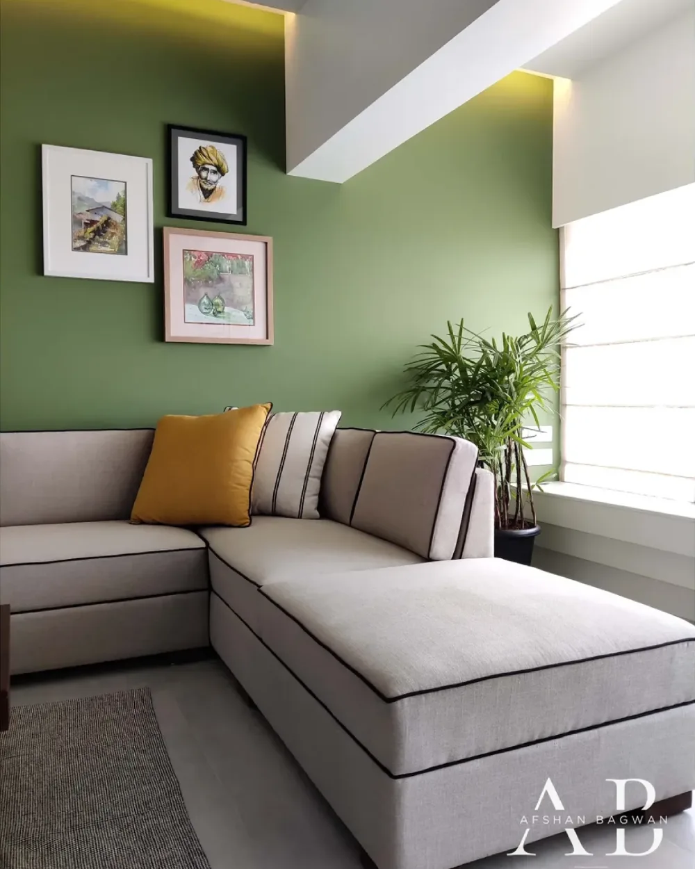 Small green living room with neutral sectional sofa, mustard cushion, houseplant, and framed artwork