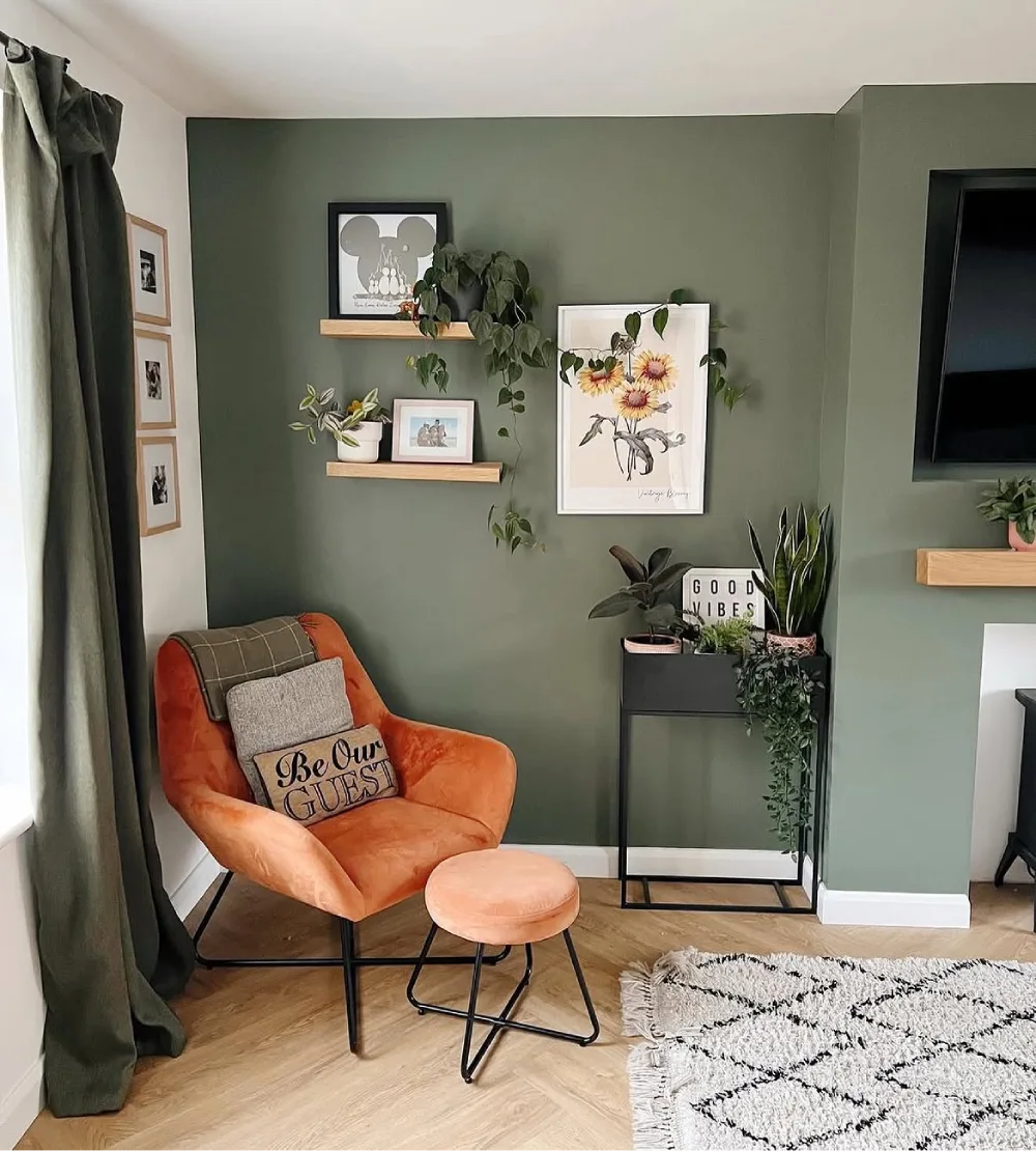 Sage green living room with orange velvet armchair, floating shelves, plants, and wood flooring