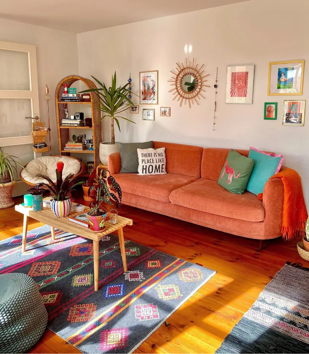 Colorful living room with coral sofa, patterned rug, plants, and eclectic wall decor