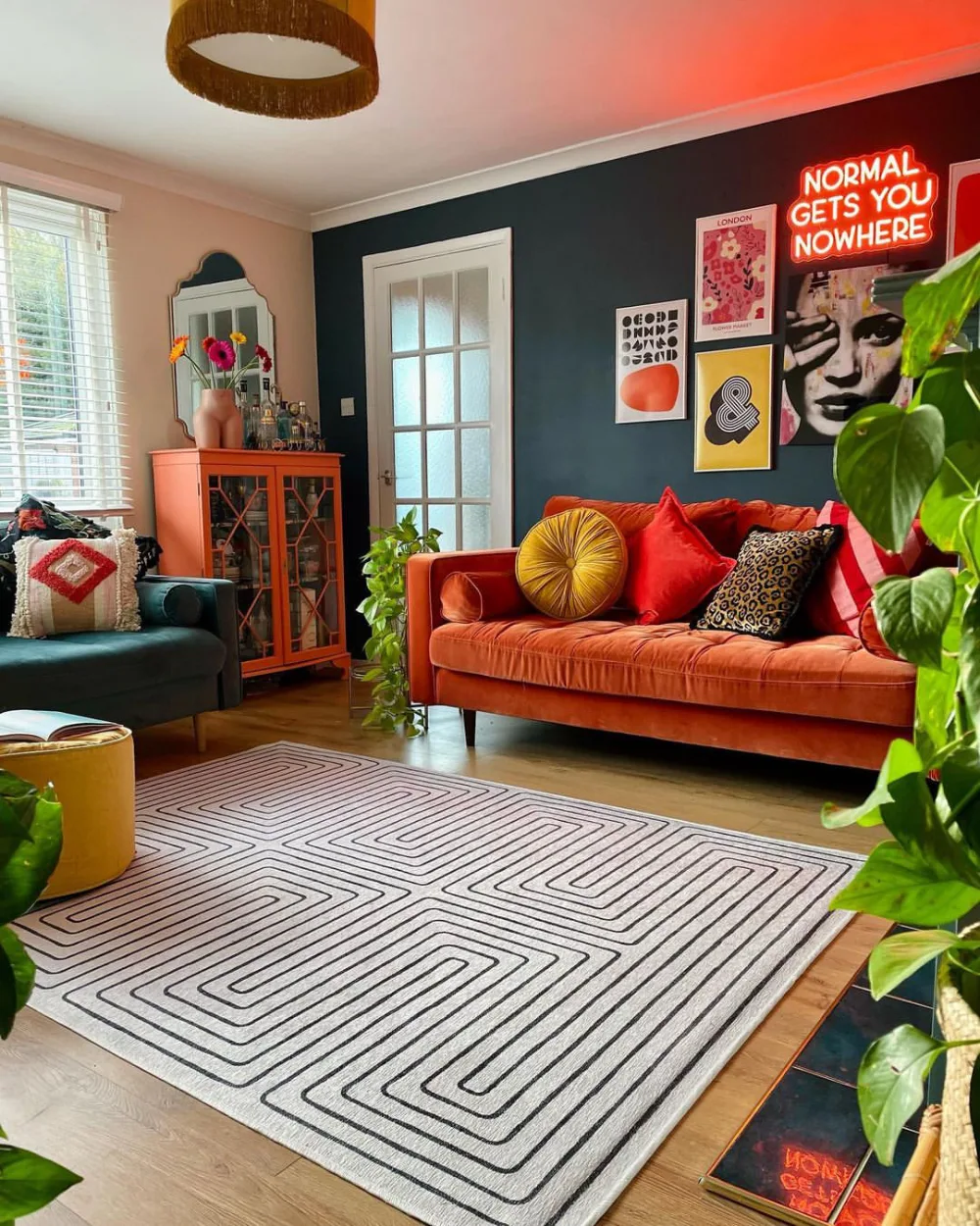 Living room with dark blue accent wall, orange sofa, colorful artwork, and plants