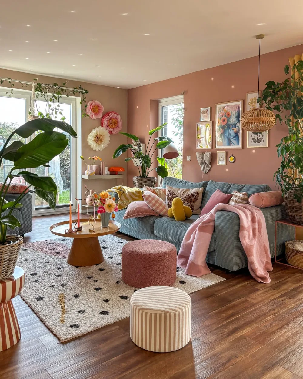 Blush pink living room with blue sofa, colorful pillows, plants, and woven pendant light