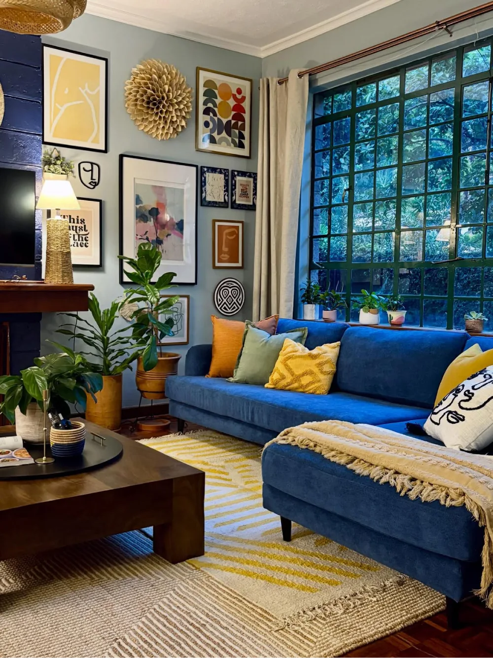 Blue living room with colorful gallery wall, plants, and velvet sectional sofa