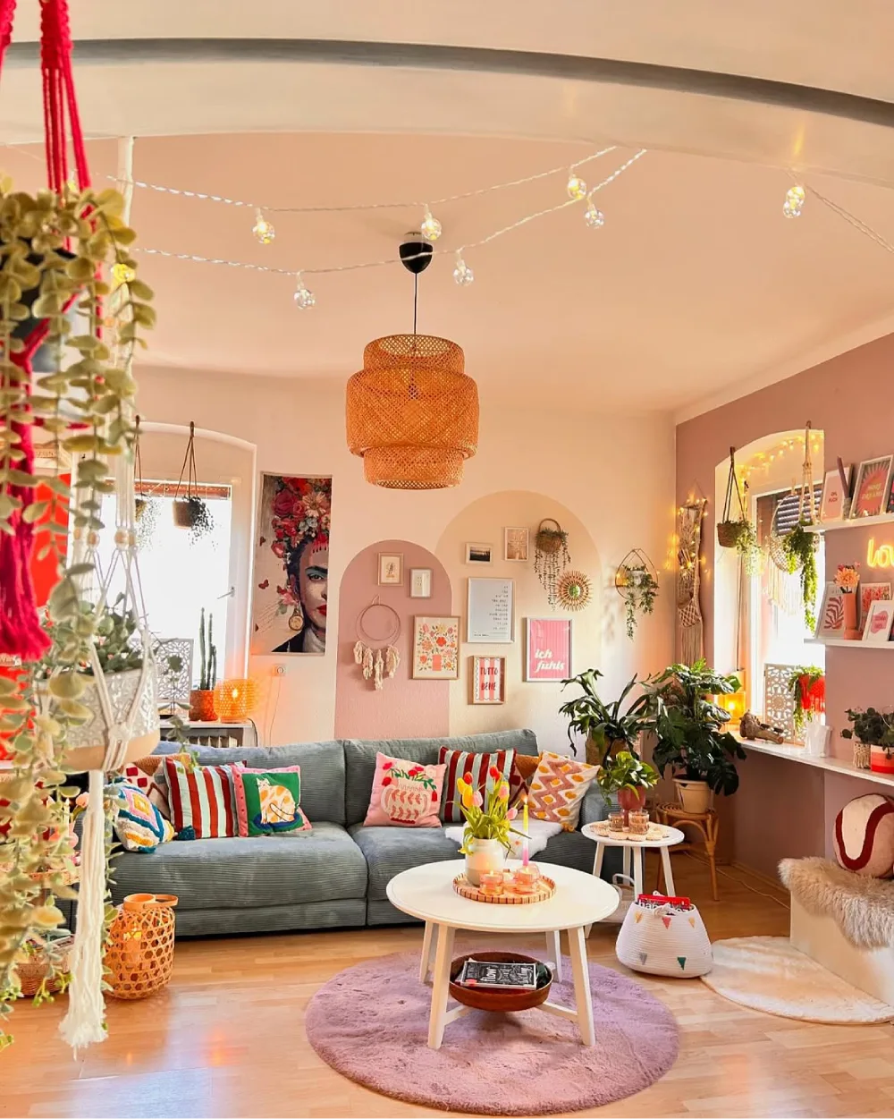 Eclectic pink living room with gallery wall, colorful pillows, plants, and string lights