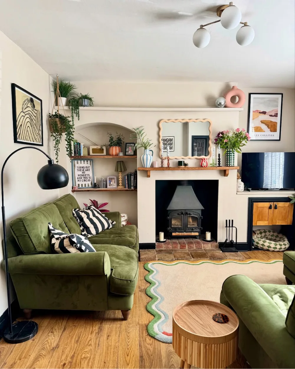 Cozy green living room with fireplace, built-in shelves, patterned rug, and velvet sofa