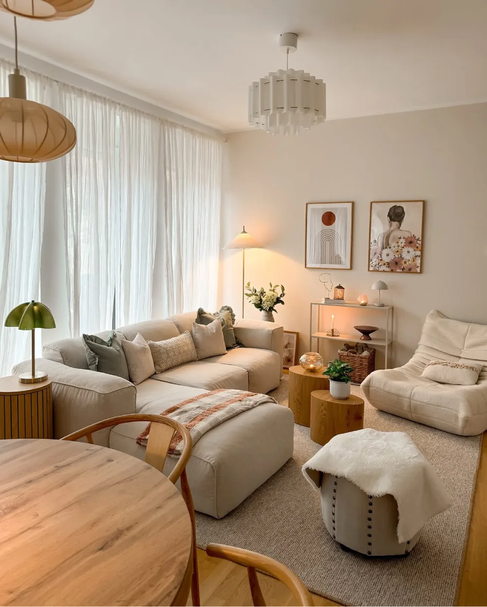 Soft neutral living room with cream seating, wood tables, layered lighting, and sheer curtains