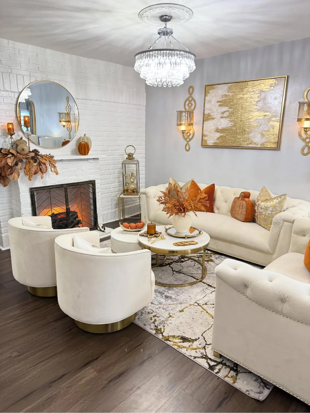 Elegant white living room with gold accents, crystal chandelier, fireplace, and autumn decor