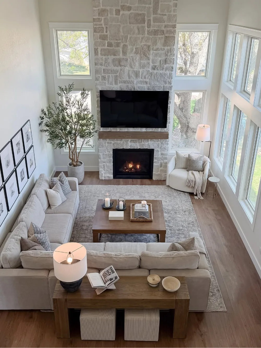 Spacious neutral living room with stone fireplace, large windows, sectional sofa, and wood accents