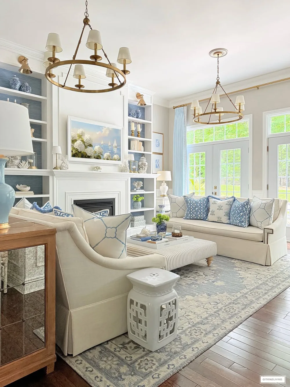 Elegant white living room with blue accents, built-in shelves, and brass lighting