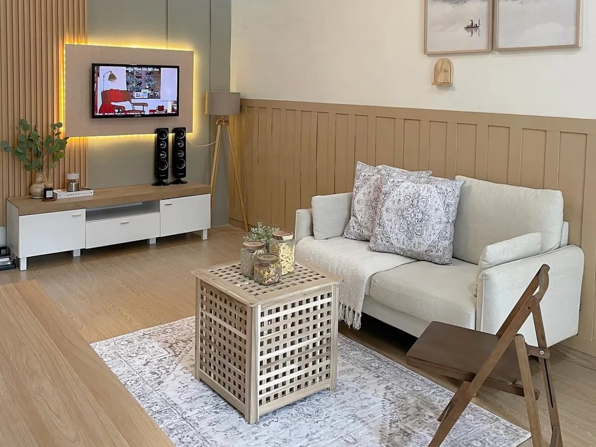Warm neutral living room with a cream sofa, wood paneling, patterned rug, framed artwork, and a woven coffee table.