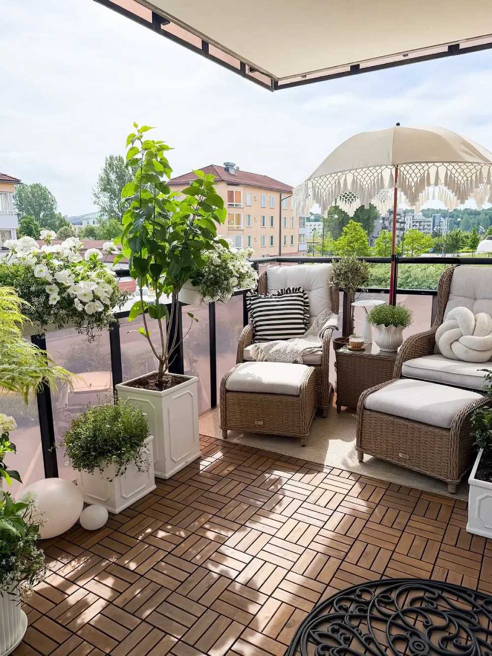 spacious balcony with wicker chairs, flowers, and a fringed umbrella