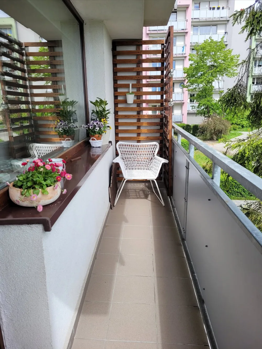 narrow balcony with white wicker chair, wood privacy screen, and flowers
