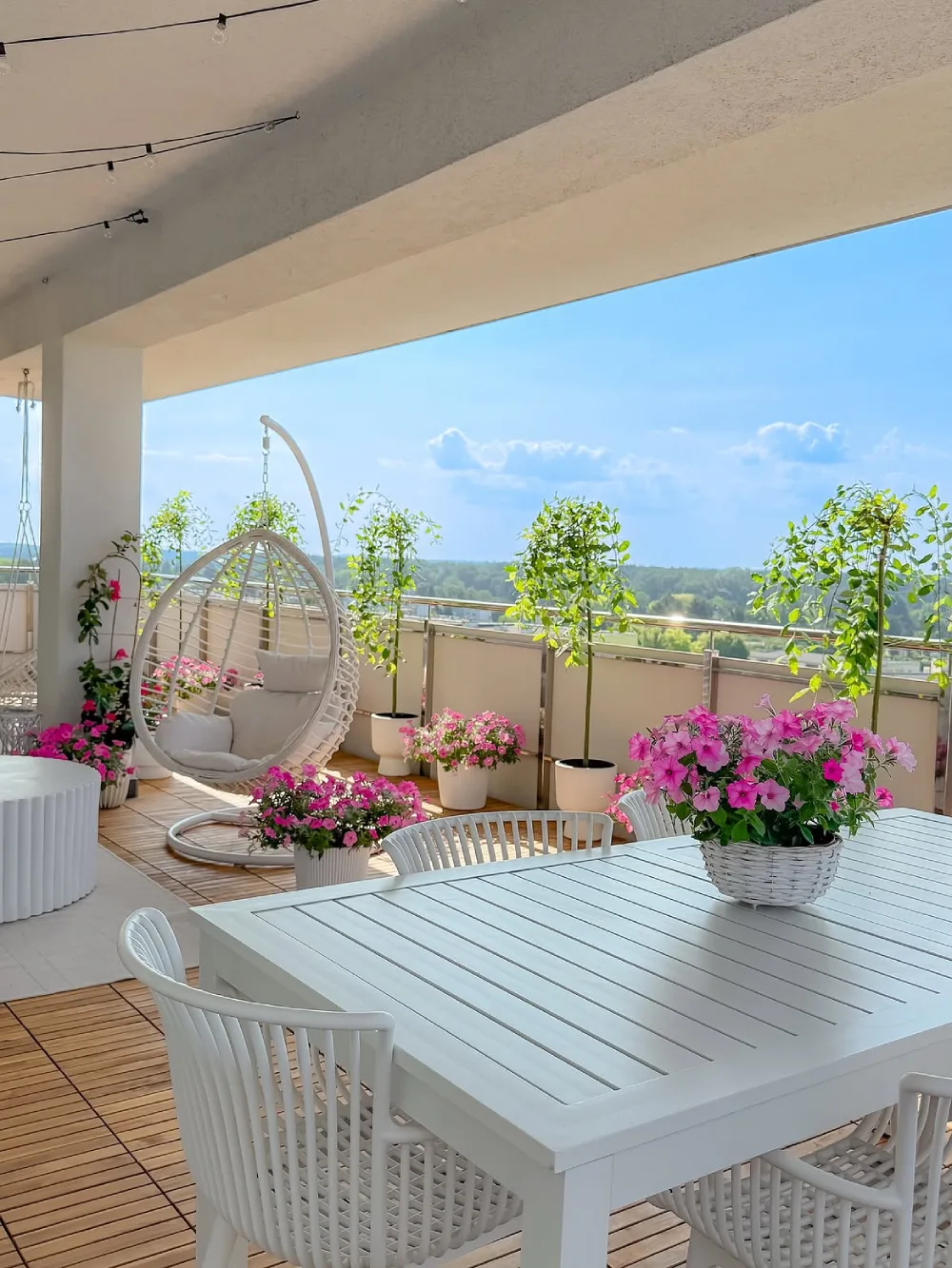 bright balcony with white dining table, wicker chairs, and pink flowers