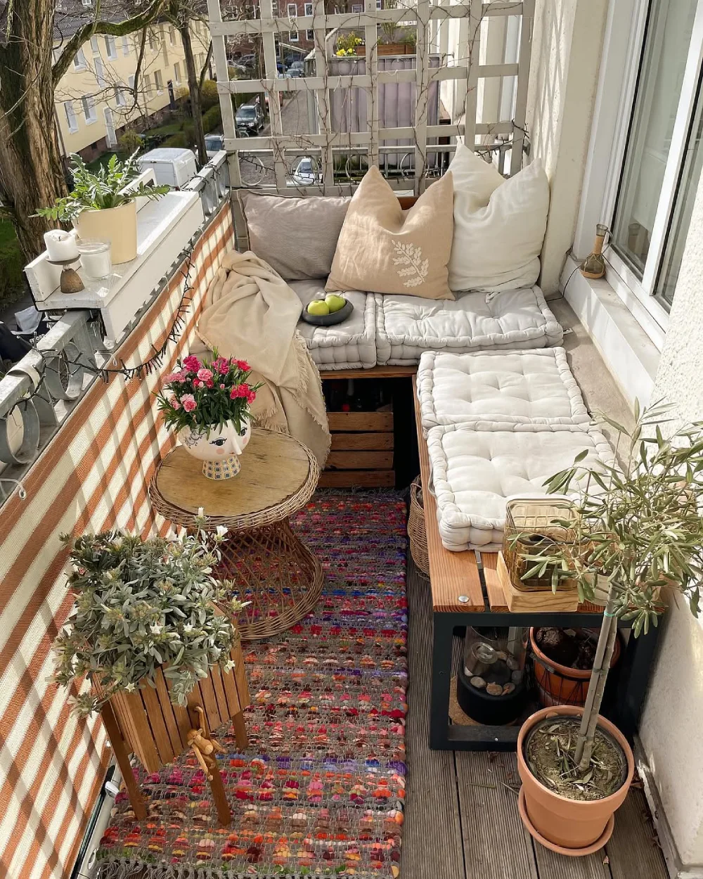 cozy balcony with cushioned seating, colorful rug, and potted plants