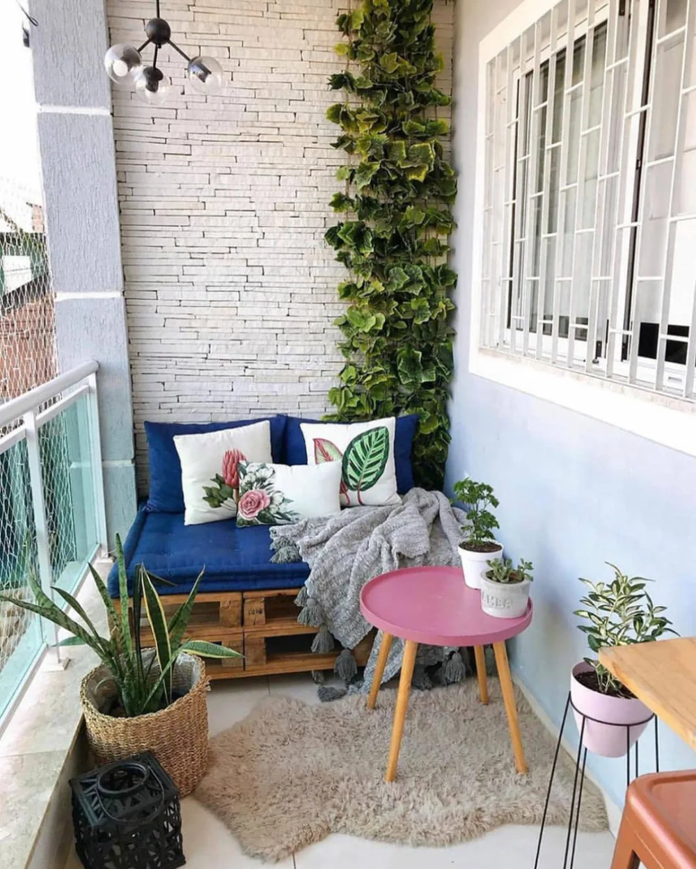 small balcony with blue sofa, pink table, plants, and patterned cushions