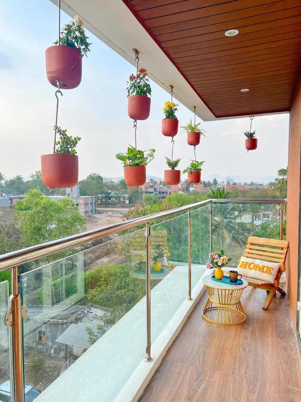balcony with hanging terracotta planters, wooden chair, and glass railing