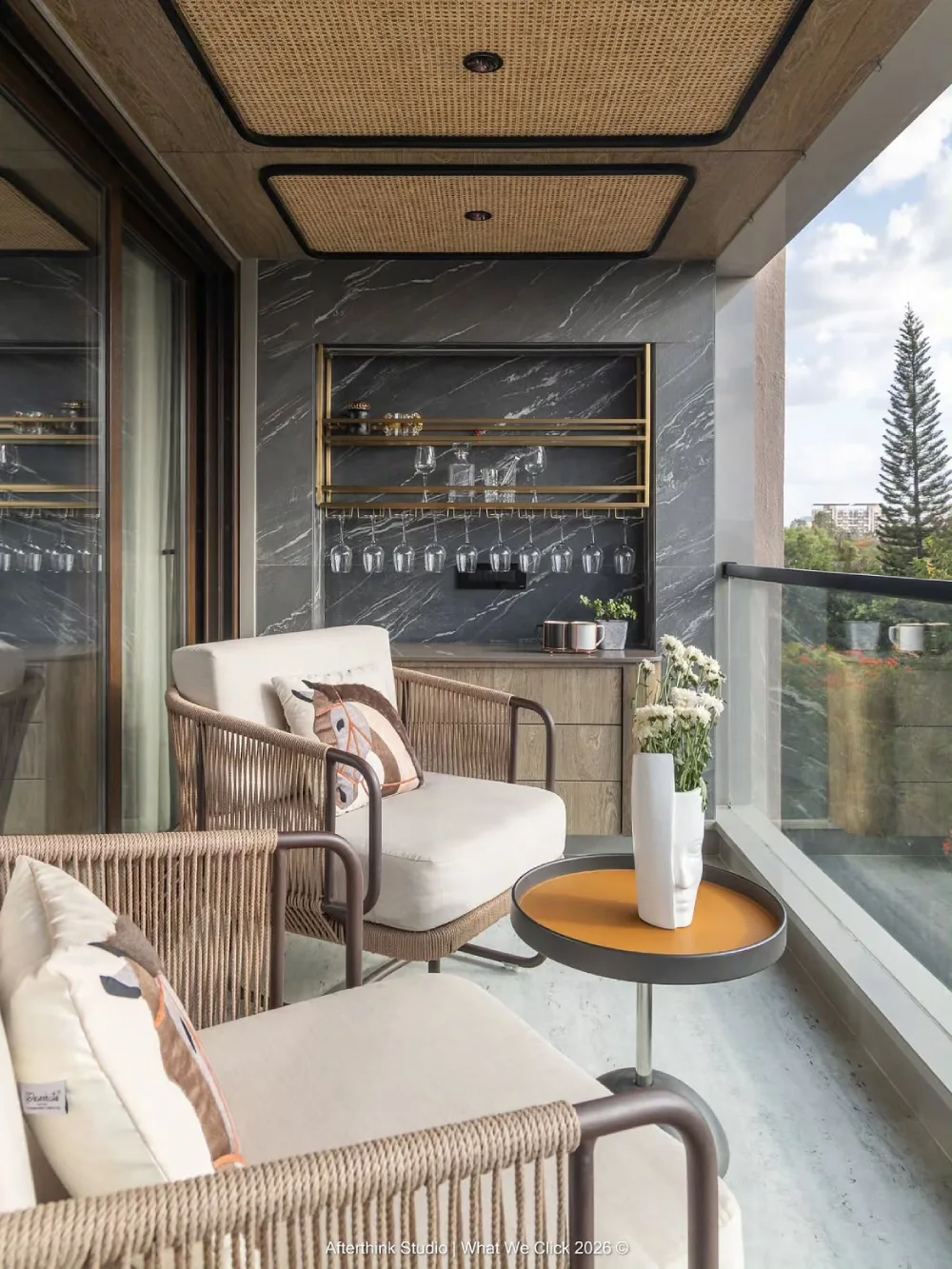 stylish balcony with woven chairs, bar shelving, dark wall, and small round table