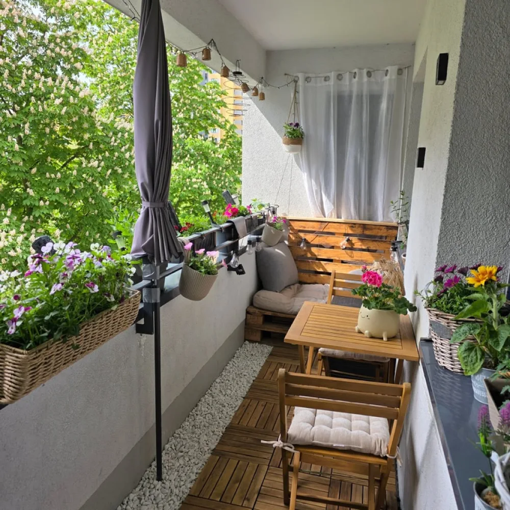 balcony dining corner with wooden table, chairs, flowering plants, and privacy screen