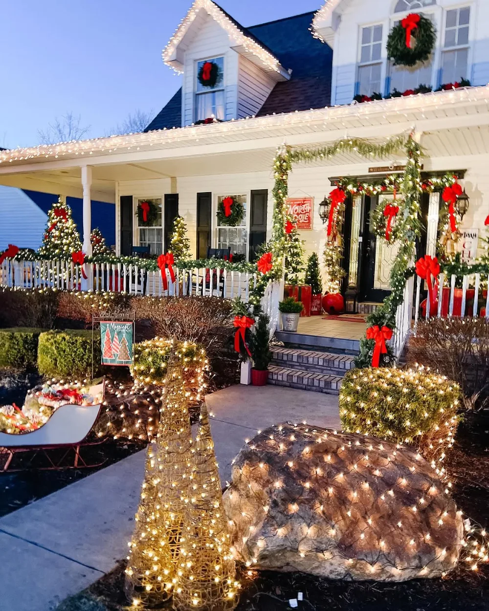 Christmas-decorated front yard with glowing trees, garlands, bows, and warm lights