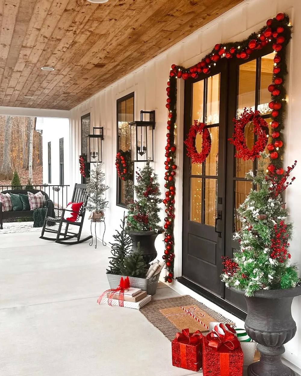 Covered porch with black double doors framed by red Christmas ornaments and berry wreaths