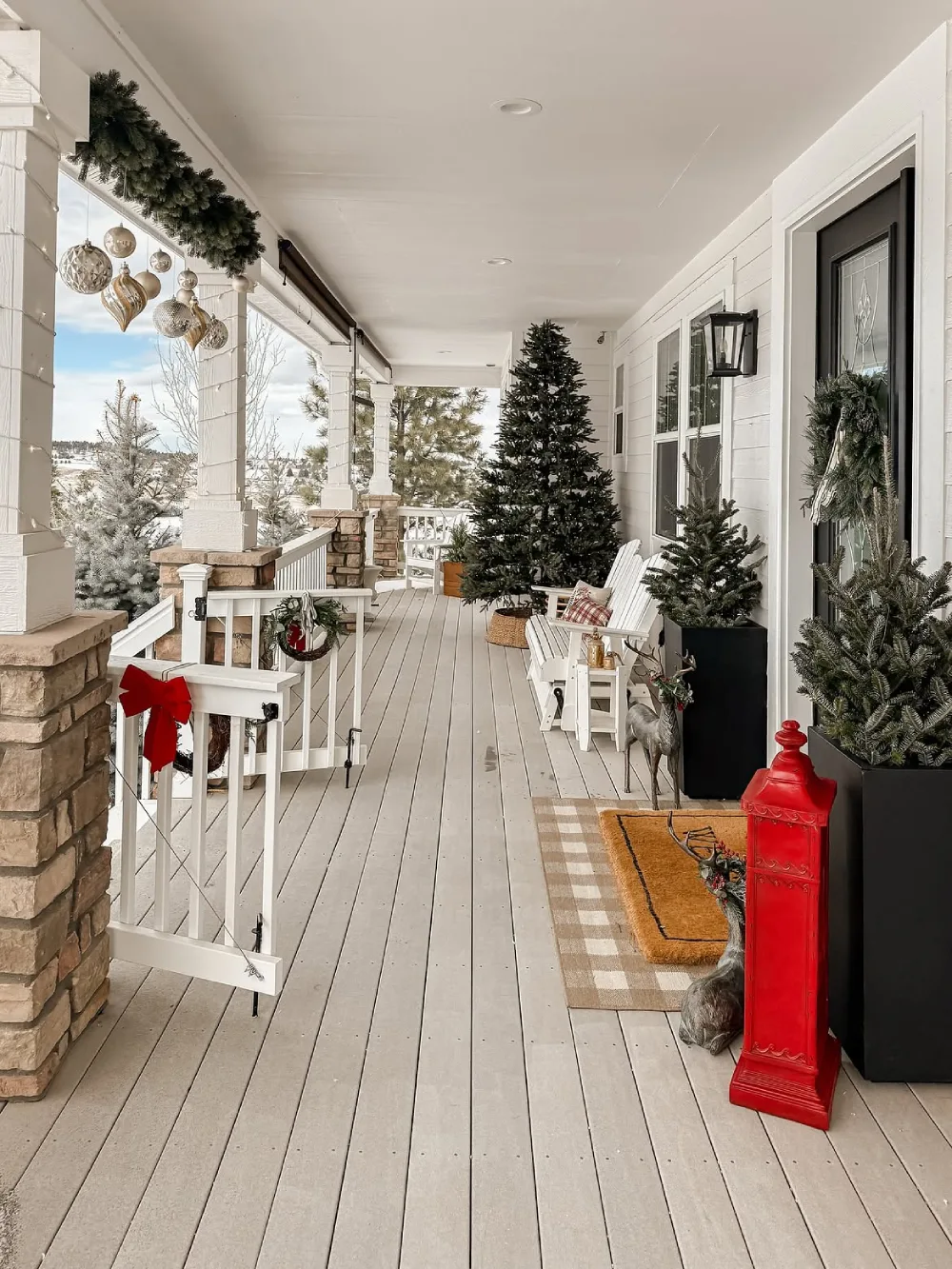 Snowy front porch decorated with evergreen trees, Christmas wreaths, and red accents