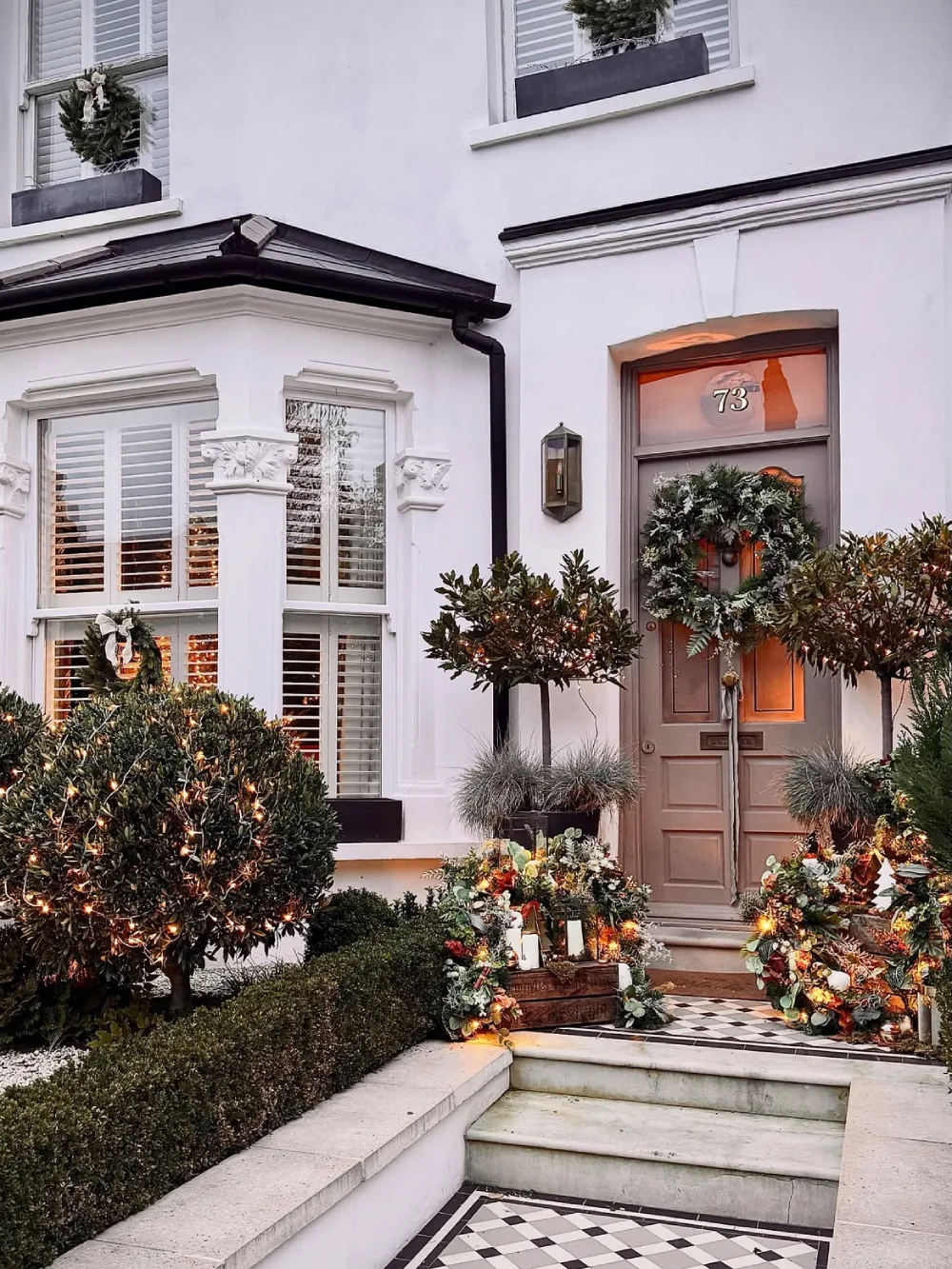 Elegant townhouse entrance with a Christmas wreath, illuminated shrubs, and seasonal planters