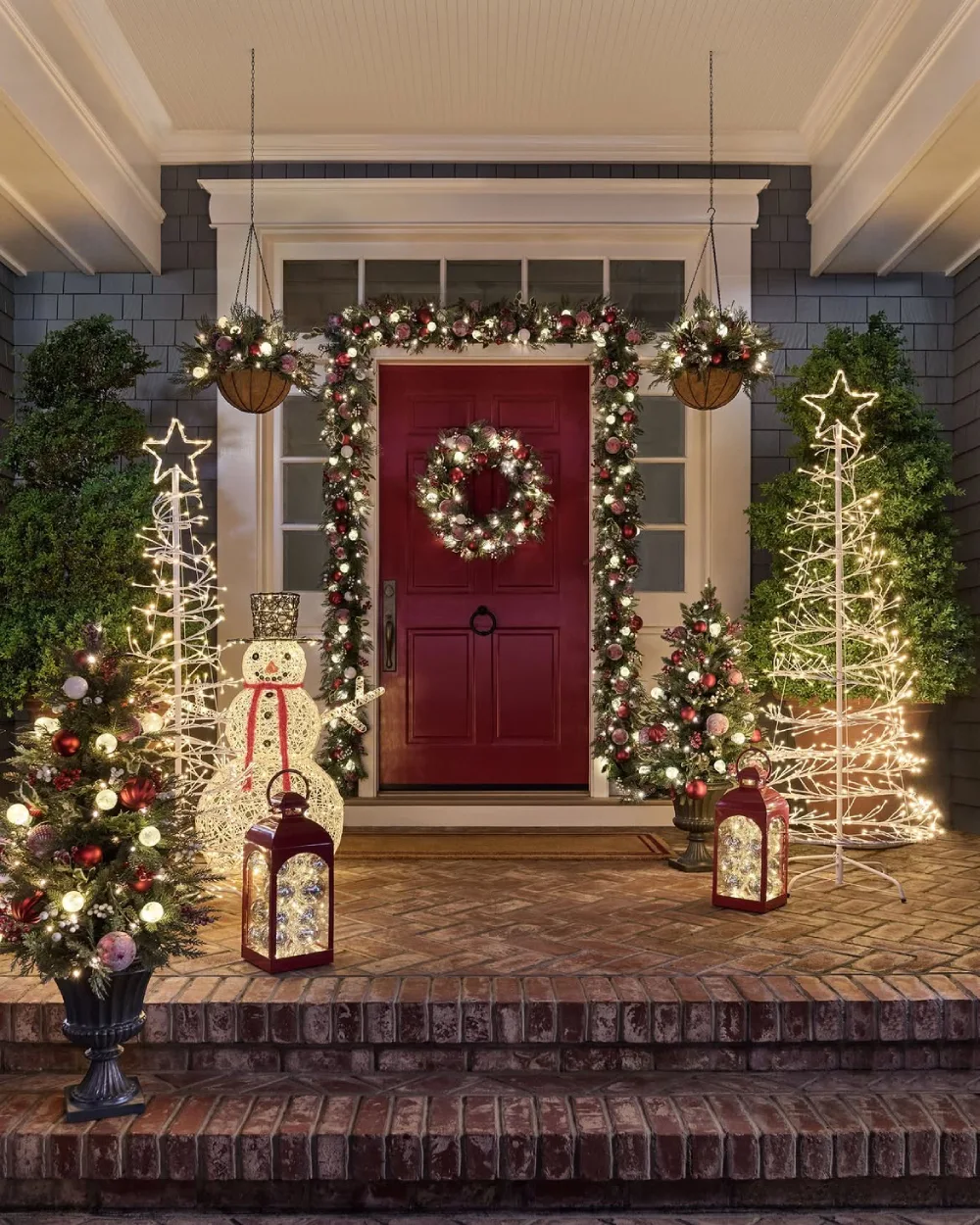 Front porch with red door, Christmas wreath, illuminated trees, and festive lanterns