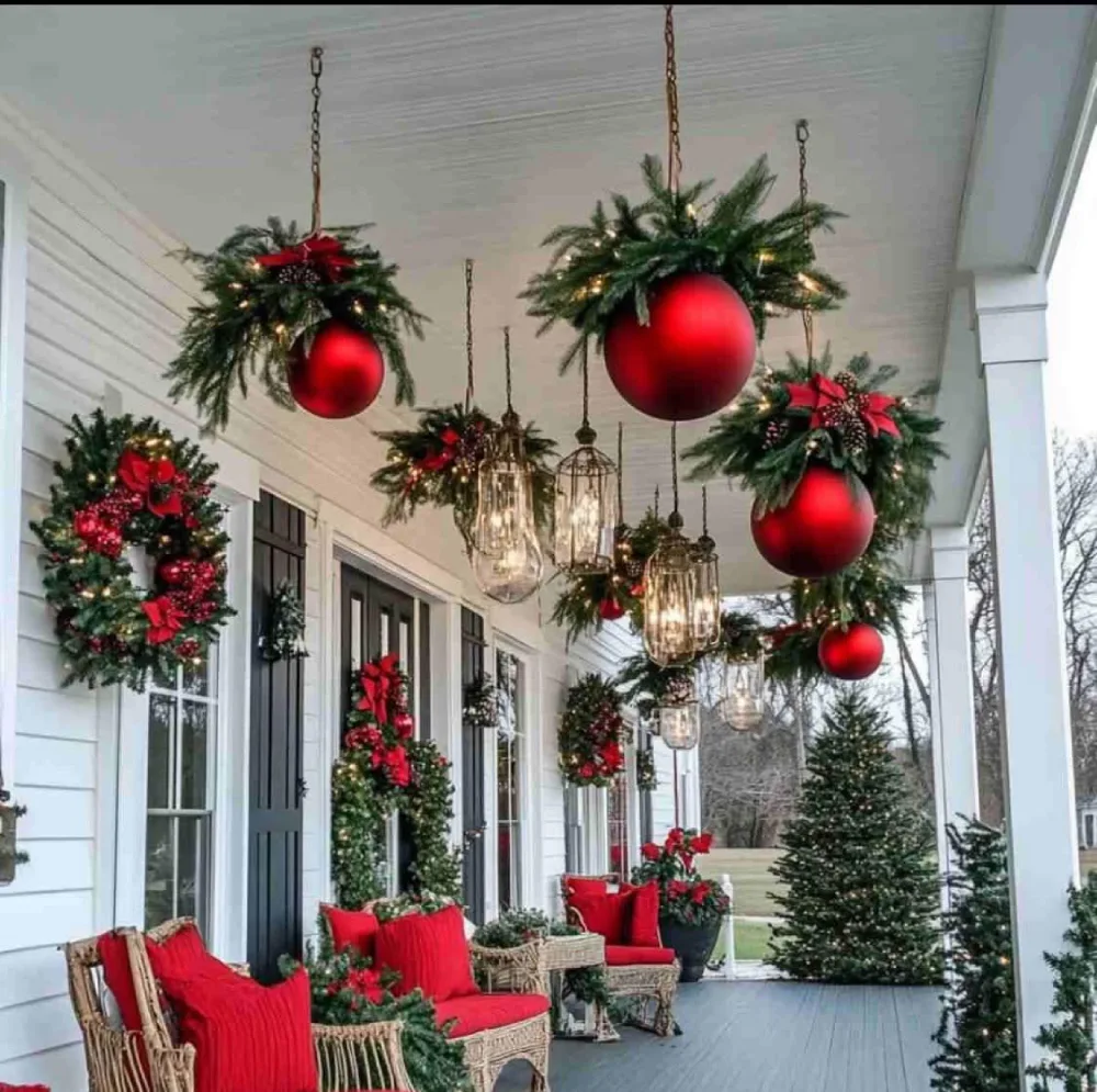Covered porch decorated with hanging oversized red Christmas ornaments and evergreen wreaths