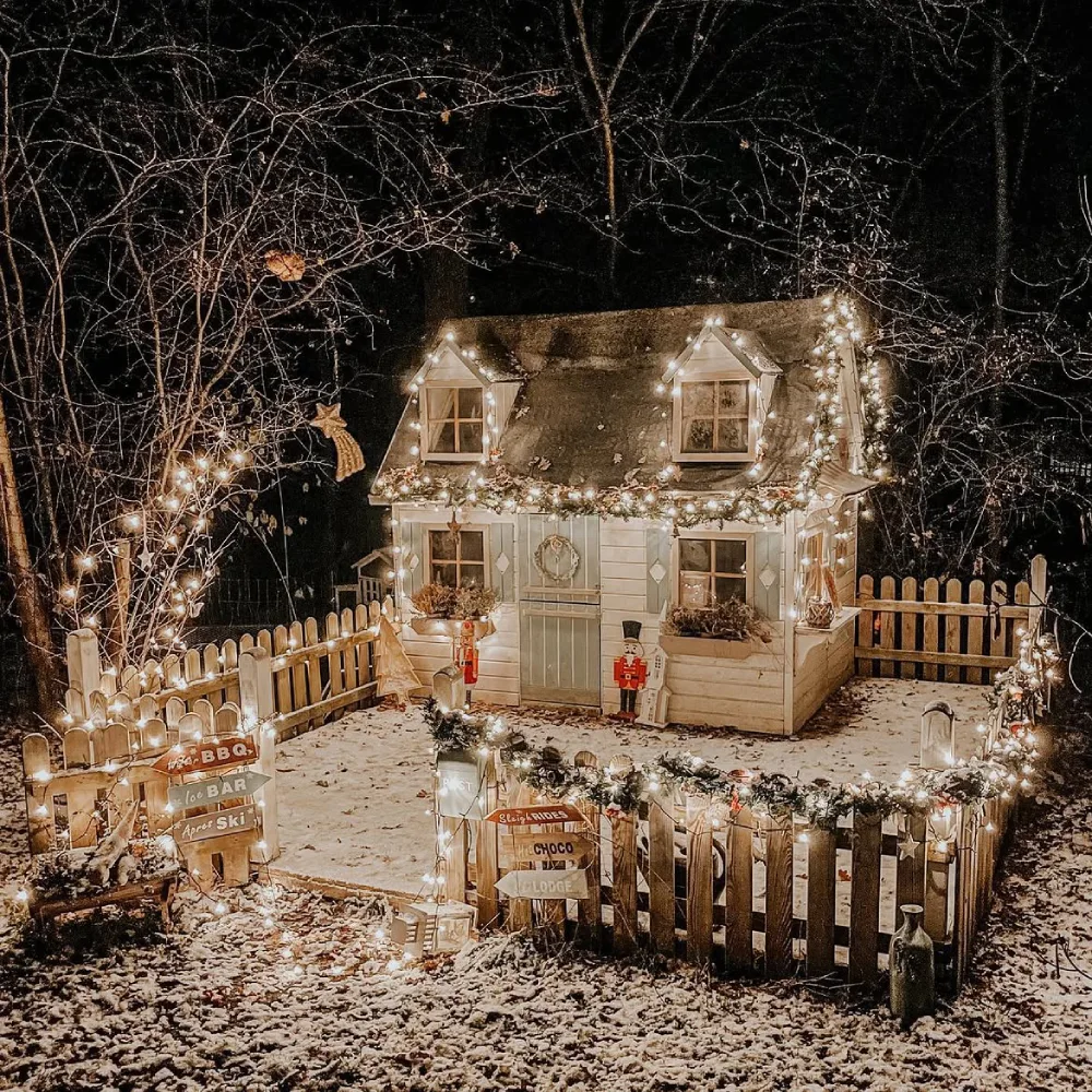 Small cottage covered in snow and decorated with warm Christmas lights and festive signs