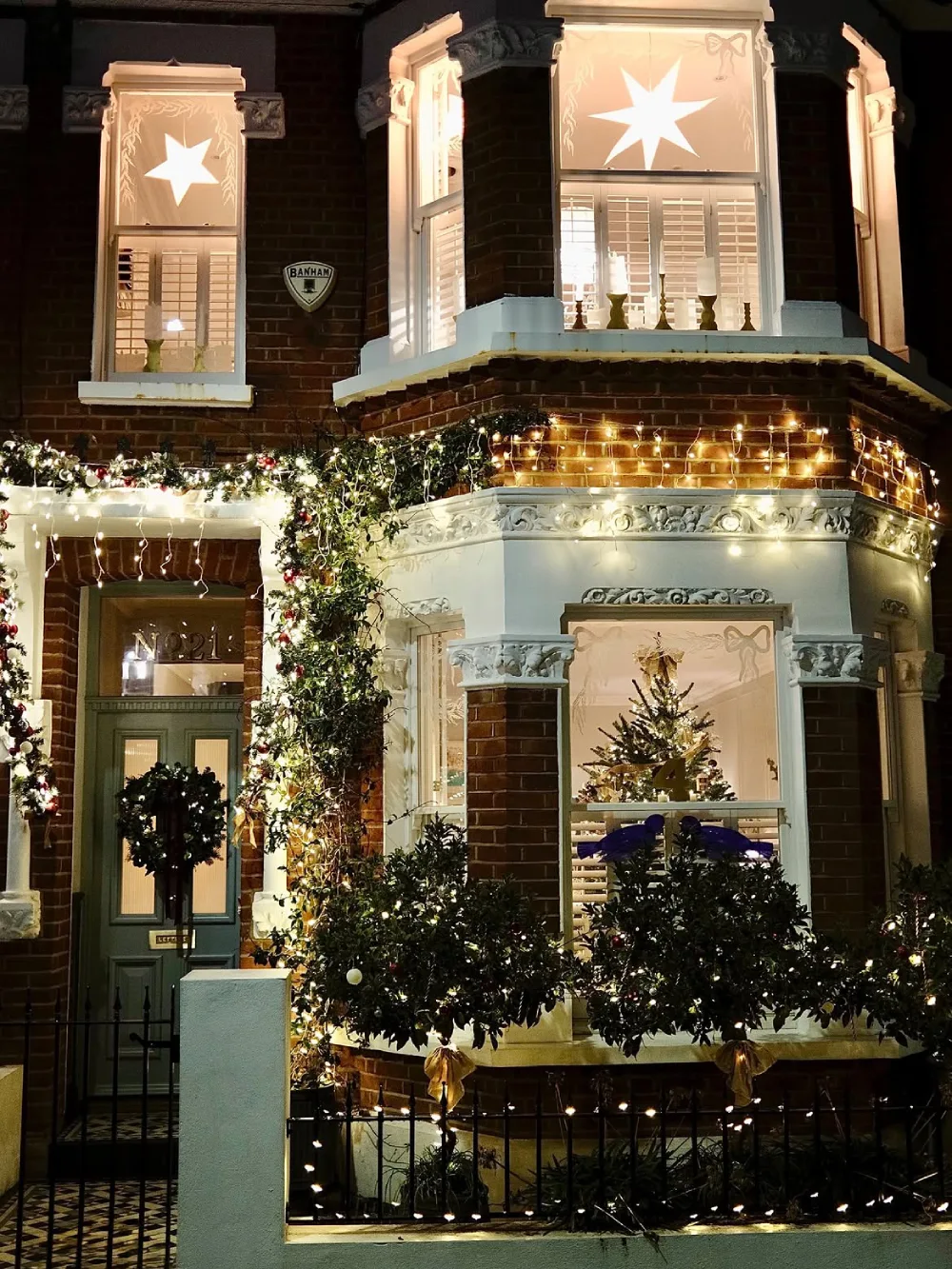 Brick townhouse decorated with Christmas lights, greenery, and glowing star window decorations