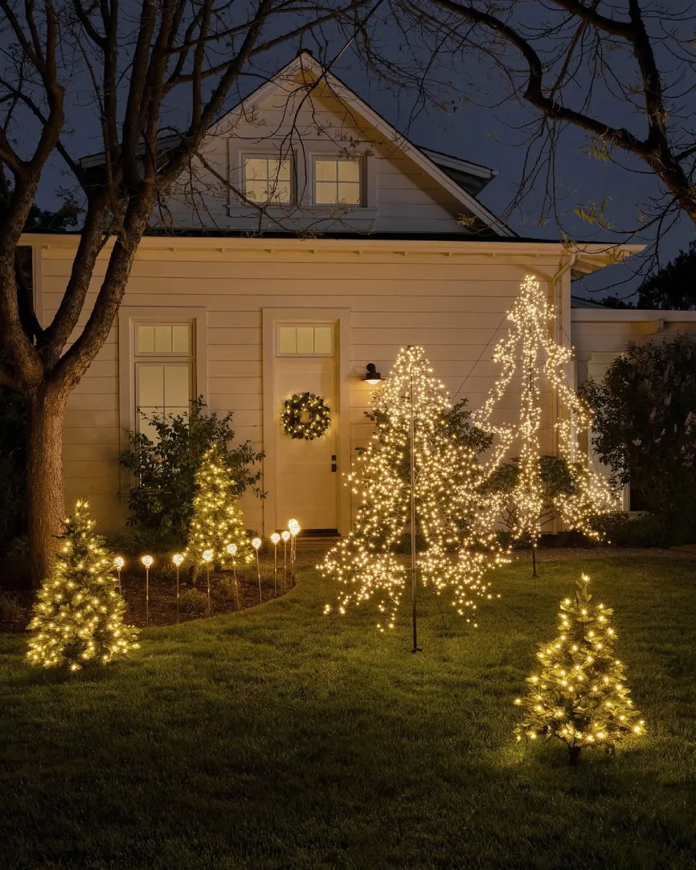 Outdoor Christmas tree glowing with warm lights beside a home at night