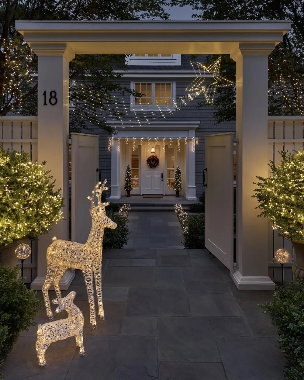 Elegant gated home decorated with Christmas lights, glowing shrubs, and illuminated reindeer