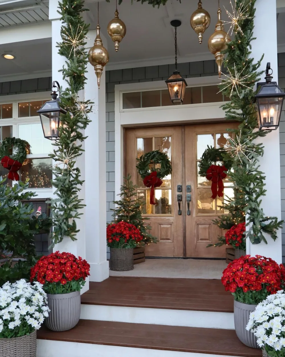 Double front doors framed with evergreen garlands, gold ornaments, lanterns, and red flowers
