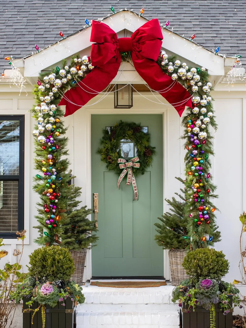 Christmas doorway decorated with oversized red bow, colorful ornaments, and evergreen garland