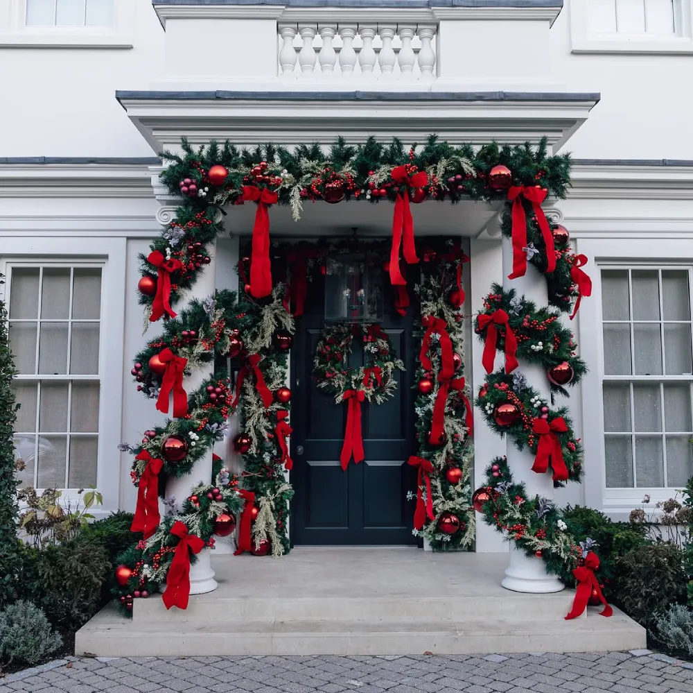 Elegant front entrance decorated with evergreen garland, red bows, ornaments, and wreaths